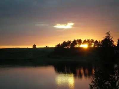 a sunset over a lake with the sun setting at Villa Alicante & SPA in Zujūnai