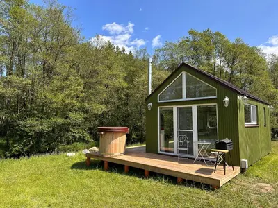 a green tiny house with a deck in a field at ALANTOS ŽIRGAI Holiday Villas sauna or hottube additional price in Alanta