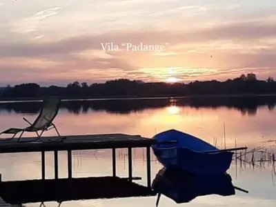 a dock with a chair and a boat on a lake at Kaimo Vila “Padange” in Kančėnai