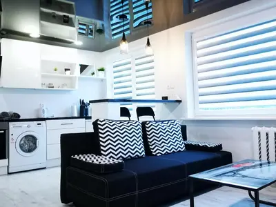 a living room with a black couch and a kitchen at Black & White Studio in Anykščiai