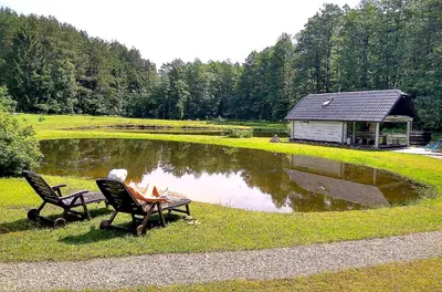 a person sitting on a bench in front of a pond at White homestead in Sumiliszki