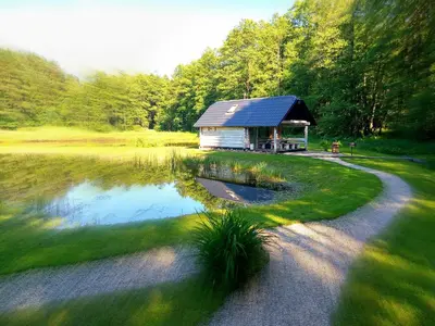 a small building next to a pond with a house at White homestead in Sumiliszki
