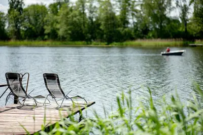 two chairs on a dock with a boat in the water at VieniKrante in Utena