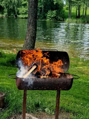 a fire in a grill in front of a lake at Namukas su ežero pakrante Trakai ,Viesų vila in Salkininkai
