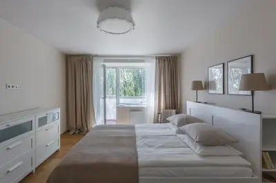 a white bedroom with a large bed and a window at Sun City Apartment in Šiauliai