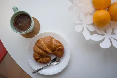 a plate with a croissant and a cup of coffee and oranges at Svajonių apartamentai in Druskininkai