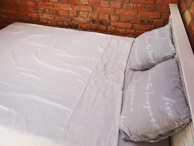 a bed with white sheets on it next to a brick wall at Little Provence Home in Vilnius