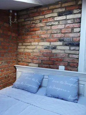 a bed with two blue pillows in front of a brick wall at Little Provence Home in Vilnius
