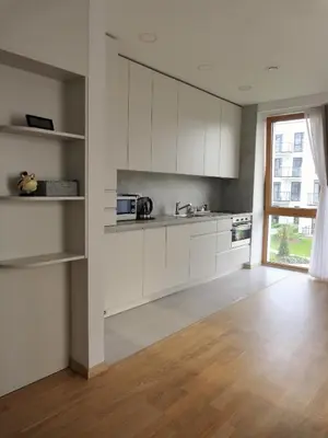 a kitchen with white cabinets and a wooden floor at Elzbietos centro apartamentai in Vilnius