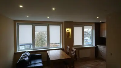 a living room with a table and three windows at Anyksciai nakvyne in Anykščiai