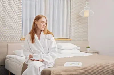 a woman sitting on a bed holding a cup of coffee at Goda Hotel & Spa in Druskininkai
