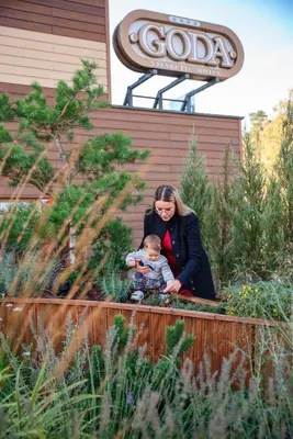a woman holding a child in front of a garden at Goda Hotel & Spa in Druskininkai