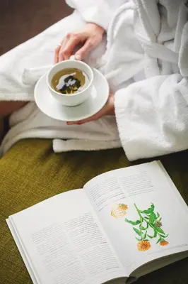 a woman with a cup of coffee and a book at Goda Hotel & Spa in Druskininkai