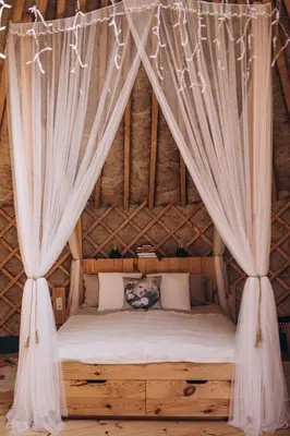 a bed in a thatched room with curtains at VasaRojaus Jurta in Birštonas