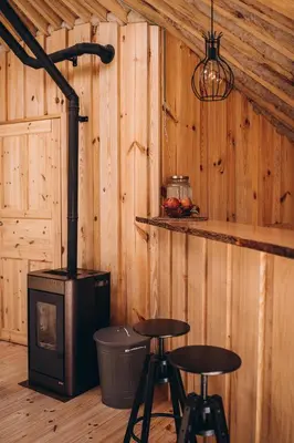 a room with a stove and two bar stools in a cabin at VasaRojaus Jurta in Birštonas