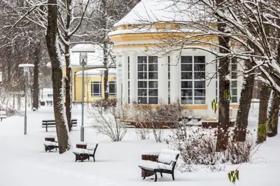 a snow covered park with benches in front of a building at Relax apartments near Egle in Druskininkai