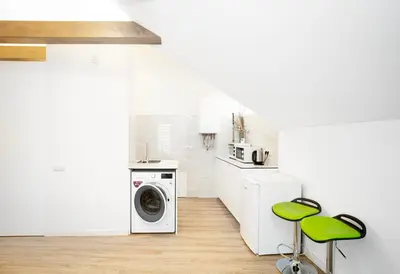 a white kitchen with a washing machine and green stools at Kaunas Castle Apartments - Studio in Kaunas