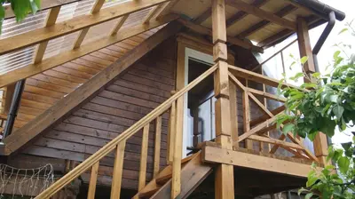 a log cabin with a wooden staircase leading up to a balcony at Namelis prie Magnolijos in Druskininkai