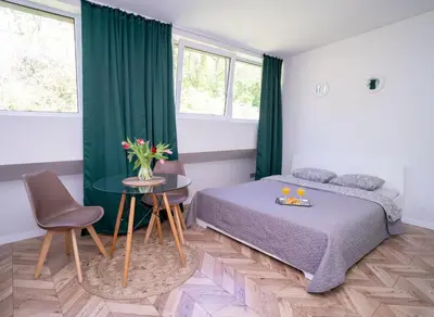a bedroom with a bed and a table and two windows at House 22A Studio Apartments in Kaunas