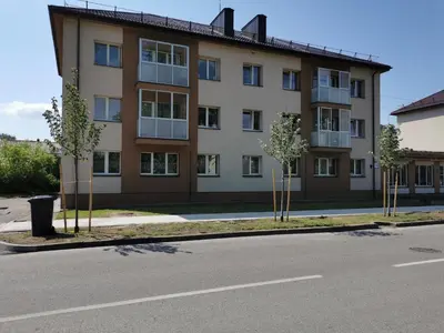 a building with trees in front of a street at Central Apartments Nojus in Druskininkai