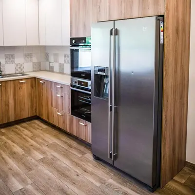 a stainless steel refrigerator in a kitchen with wooden cabinets at Sodyba Pelėdų medus in Vainekoniai