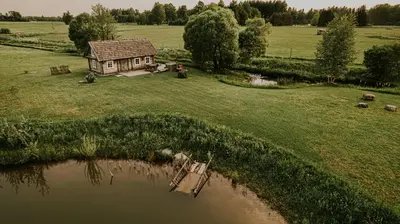 a small house in a field next to a pond at Vienkiemio Oazė - Pasakų namelis in Galvokai