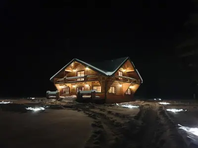 a log cabin lit up in the snow at night at Poilsio ir sveikatinimo sodyba Pušų Šlamesy in Vilnius