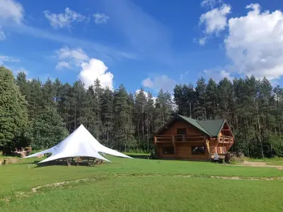 a tent in a field next to a log cabin at Pušų Šlamesy in Vilnius
