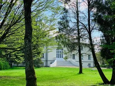 a white house with trees in the foreground at Botanical Manor Apartment in Kaunas