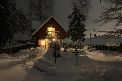 a house with lights in the snow at night at Rustic private Cabin in woods w/ Sauna & Pool in Vilnius