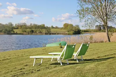 two chairs and a picnic table on the grass near a lake at Lavender Village in Kiemeliai