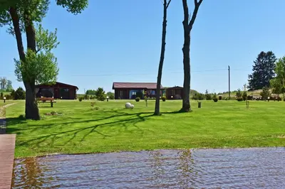 a house in a field with trees and a body of water at Vastapo Vilos in Kaniūkai