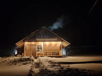 a log cabin with lights in the snow at night at Namelis prie ežero in Miežoniai