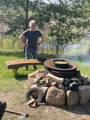 a man standing next to a picnic table and a grill at Gintaro sodyba in Lazdijai