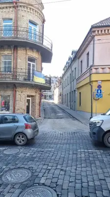 two cars parked on a cobblestone street with buildings at RBRoom in Vilnius