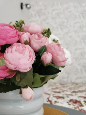 a white vase filled with pink flowers on a table at Upės apartamentai in Biržai