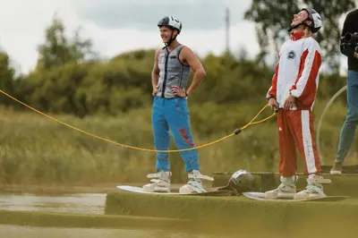 two men standing on surfboards with a dog on a rope at Wakepond atostogų slėnis in Anykščiai