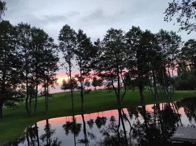 a sunset on a golf course with trees and a pond at Poilsio namas Vydautiškių slėnis in Sudervė