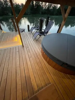 a wooden deck with a table and chairs on the water at Gintaro pirtelė in Lazdijai