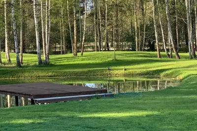 a pond with a dock in the middle of a golf course at Forest house for family in Lebeniškiai