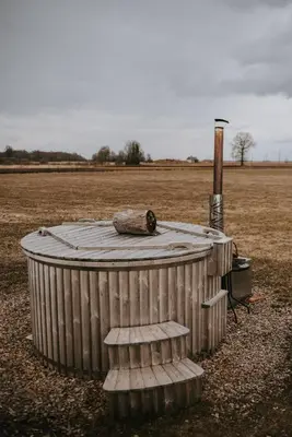 a bird sitting on top of a wooden tub in a field at Vienkiemio oazė - Skandinaviškas namelis su vaizdu į tvenkinį in Galvokai