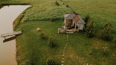 a small house in a field next to a body of water at Vienkiemio oazė - Skandinaviškas namelis su vaizdu į tvenkinį in Galvokai