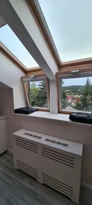 a attic room with two windows and a radiator at Jaukus butas Vilniuje Žvėryno rajone in Vilnius