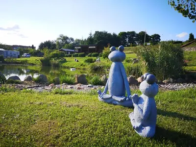 two statues of people sitting on the grass near a pond at Camp Genys in Jurbarkas