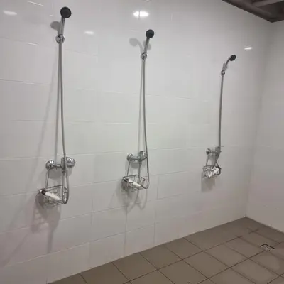 a white tiled bathroom with three shower stalls at Camp Genys in Jurbarkas