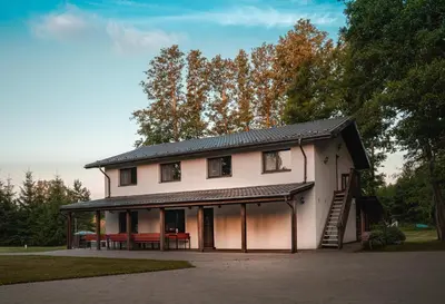 a large white house with a porch and a table at Vėjo Malūnų sodyba - vila in Paserninkai