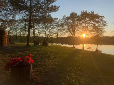 a sunset over a lake with flowers in a park at Kedras Glamping - Pod tipo nameliai in Prapuntai