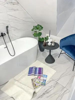 a room with a bath tub and a table and a blue chair at Kamurke - Apartamentai in Šiauliai