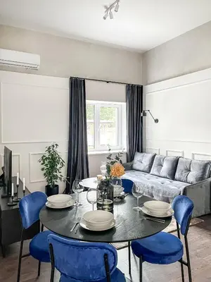 a living room with a table and blue chairs at Kamurke - Apartamentai in Šiauliai