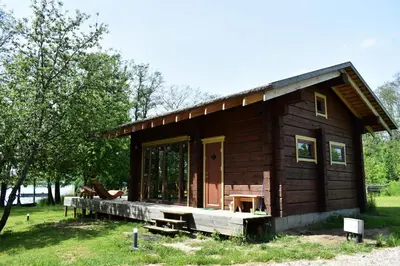 a small log cabin with a porch and a door at Kaimukas - namelis prie ežero keturiems in Dvarčėnai